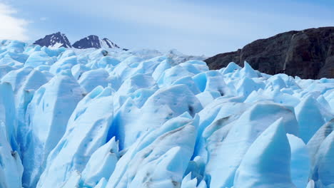 Blauer-Sonnenbeschienener-Schmelzender-Gletscher,-Tiefe-Gletscherspalten,-Ferne-Berge