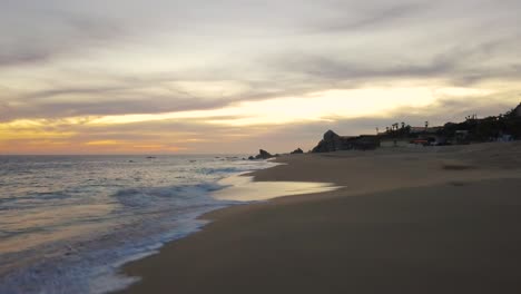 Waves-crashing-onto-an-empty-beach-in-Cabo-San-Lucas,-Mexico,-at-sunset