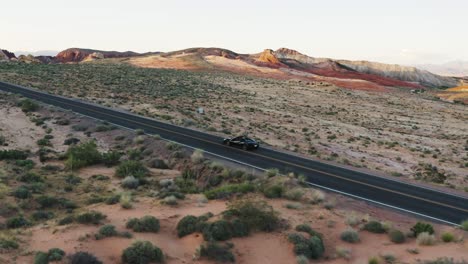 Black-luxury-sports-car-driving-down-a-highway-in-the-Valley-of-Fire,-Nevada,-USA,-at-sunset