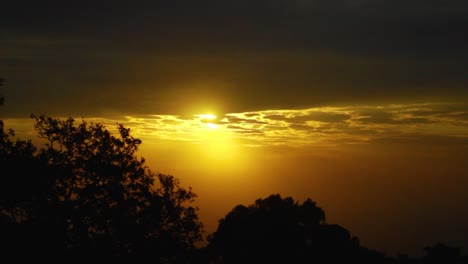 Ein-Zeitraffer-Der-Sonne,-Die-In-Einer-Afrikanischen-Ebene-über-Einem-Baumbedeckten-Vordergrund-Mit-Wolkendecke-Aufgeht