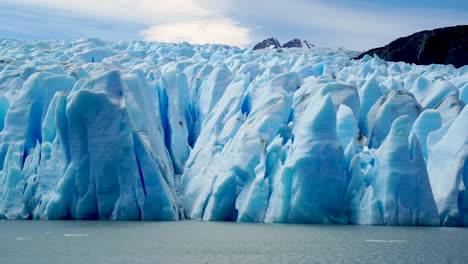 Blue-sunlit-glacier-with-large-crevasses-melting,-distant-mountains