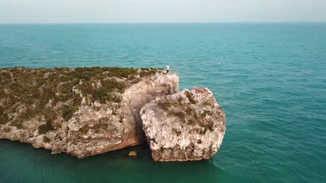 Young-male-standing-at-the-end-of-a-rocky-cliff-on-the-ocean-in-Providenciales-in-the-Turks-and-Caicos-archipelago