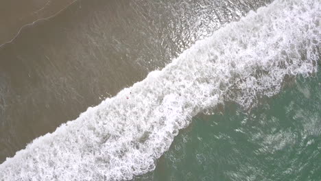 Cenital-drone-shot-flying-straight-up-over-the-splashing-waves-at-the-beach-in-Playas-General-Villamil,-Ecuador