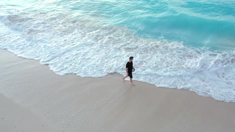Young-male-walking-along-a-sandy-beach-in-Providenciales-at-sunset-in-the-Turks-and-Caicos-archipelago