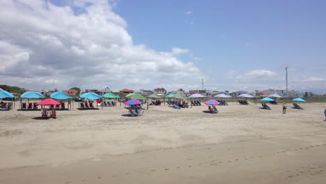 Low-close-to-the-ground-drone-flight-shot-towards-tents-and-umbrellas-with-people-in-the-town-beach-of-Playas-General-Villamil-in-Ecuador