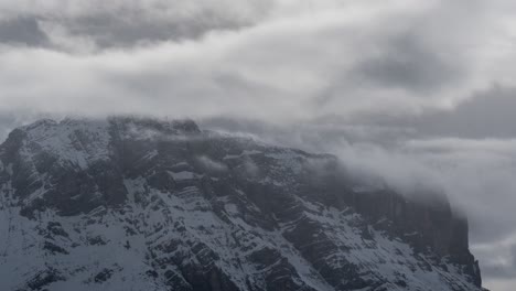 Thick-white-clouds-flowing-over-the-snow-covered-mountain-peak-in-the-Dolomites