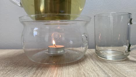 Nahaufnahme-Auf-Klarglas-Teekannenwärmer-Mit-Kleiner-Brennender-Kerze-Und-Teetasse