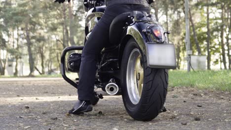 Man-dressed-up-in-professional-motorcycling-clothes-rides-chopper-during-holden-hour-in-forest-trees-in-slow-motion