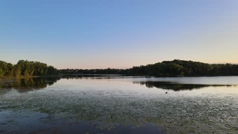 A-gental-glide-from-the-shore-line-of-tall-lush-green-grass-to-the-open-water-as-the-sun-is-setting-over-a-lake-in-Minnesota
