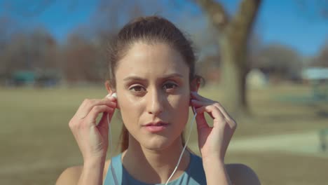 Portrait-of-Pretty-Fitness-Girl-Putting-On-Earphones-Before-Work-Out-Looking-At-Camera-With-Confidence,-Close-Up-Shot