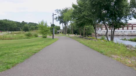 Pov-walking-along-asphalt-gray-path-along-a-city-park-in-Chippewa-Falls,-Wisconsin