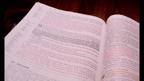 4K-clip-of-Bible-on-wooden-table-open-to-Gospel-of-John,-moving-over-while-page-is-being-turned