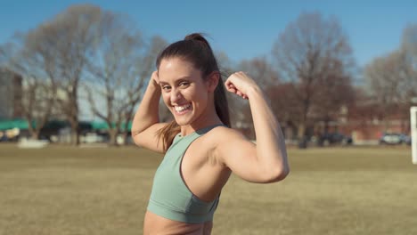 Young-Beautiful-Fitness-Woman-Flexes-Arm-Muscles-While-Turning-To-Smile-At-Camera-Feeling-Proud-Of-Her-Strength,-Power-And-Confidence-After-Workout-At-Park