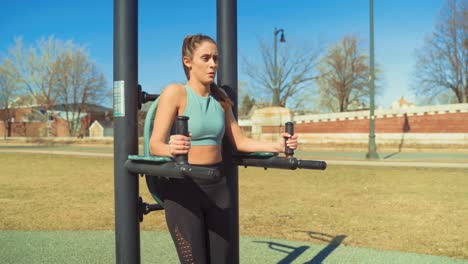 Young-Attractive-Fitness-Woman-Exercising-At-Outdoor-Gym,-Doing-Hanging-Leg-Raise-Exercise-While-Staying-Focused-And-Determined,-Wearing-Sports-Bra-And-Yoga-Pants