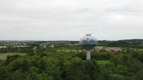 Rotating-aerial-of-water-tower-holding-water-tank,-standing-isolated-and-tall-in-lush-greenery-at-Menominee,-Wisconsin,-USA