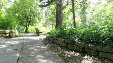 A-concrete-path-cuts-through-a-hill-lined-with-large-river-rocks-up-the-incline-to-a-bench-on-the-top-at-a-park-and-nature-preserve-in-la-crosse-wisconsin
