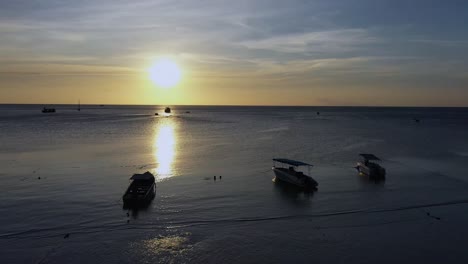 Drone-Aerial-sunset-shot-with-camera-moving-from-beach-over-calm-ocean-towards-sun-in-Koh-Tao,-Thailand
