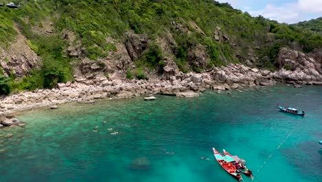Drone-aerial-shot-of-rocky-bay-with-longtails-and-coral-reef-on-Koh-Tao,-Thailand
