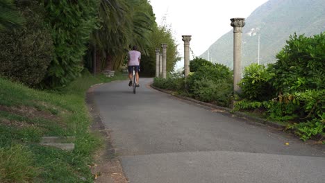 Guy-Conduce-Una-Bicicleta-De-Una-Sola-Velocidad-En-Su-Hermoso-Jardín-Rodeado-De-Naturaleza-Verde-Y-Montañas