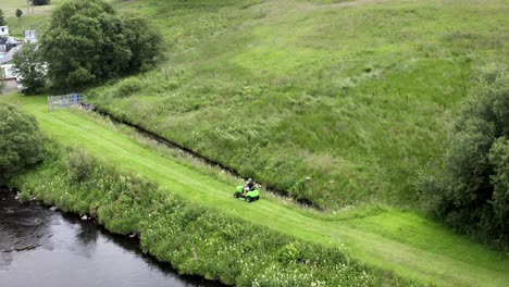 Cutting-grass-along-a-Scottish-riverside-on-a-ride-on-mower-in-summer