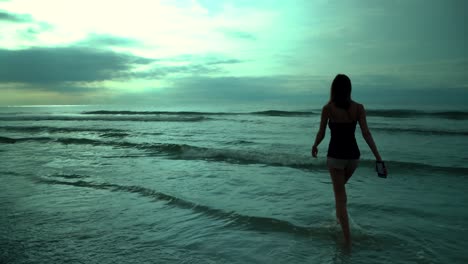 Young-woman-walking-in-the-ocean-at-sunset