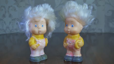 Two-Toy-Twin-Dolls-Stand-On-A-Wooden-Table