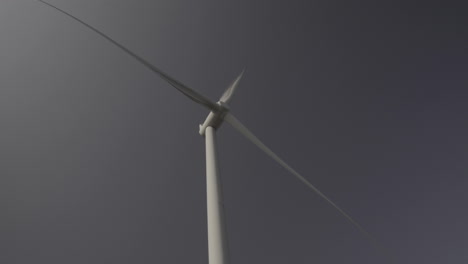 Wind-turbine-from-bellow-and-in-front,-head-spinning-with-blue-sky-background