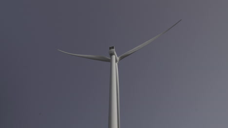 Wind-turbine-from-bellow-and-behind,-head-spinning-with-blue-sky-background