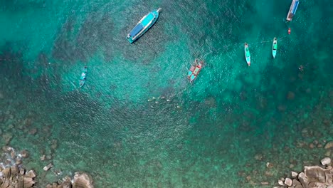 Drone-aerial-shot-above-rocky-bay-with-snorkellers-and-boats-in-water,-at-Koh-Tao,-Thailand