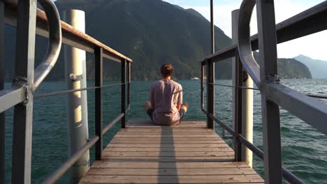 Guy-meditates-on-a-deck-near-water