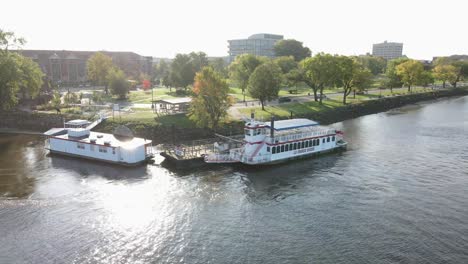 Aerial-view-from-the-water-of-a-small-cruise-ship-docked-at-riverside-park-in-La-Crosse,-Wisconsin