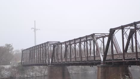 Alte-Eisenbahnbrücke-Aus-Holz-Und-Stahl-Jetzt-Ein-Wanderweg-Im-Phoenix-Park-In-Eau-Claire-Wisconsin-überquert-Den-Chippewa-River-Und-Wird-Bei-Frischem-Schneefall-Schneebedeckt