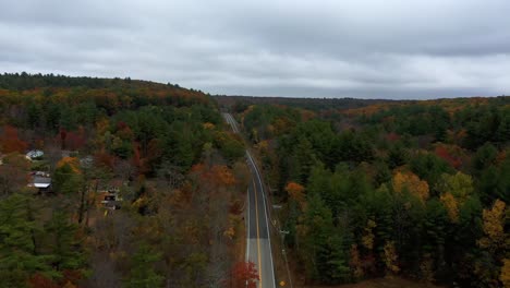 Aerial-of-lone-car-on-country-road-through-forest-in-fall,-New-England