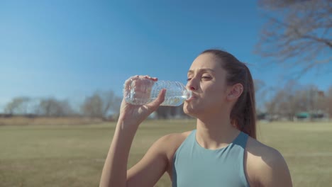 Mujer-Joven-En-Forma-Bebiendo-Agua-Embotellada-Para-Hidratarse-Antes-De-Su-Entrenamiento-Al-Aire-Libre-En-Un-Caluroso-Día-Soleado-De-Verano