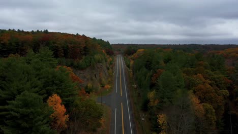 Forward-aerial-along-country-road-through-colorful-hilly-autumn-forest