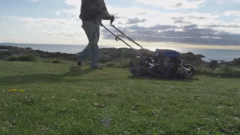 A-Man-With-A-Self-Propelled-Trimmer-Cuts-Grass-In-A-Lawn-Near-The-Sea