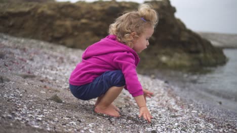 A-Cute-Girl-In-Purple-Hoodie-Playing-Pebbles-On-The-Beach---Medium-Shot,-Slow-Motion