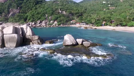 Waves-hitting-rocks-steady-shot-palm-tree-background-near-island