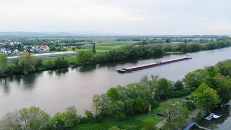 Aerial-view-of-a-Inland-waterway-shipping,-freight-transport-on-Main-river,-in-Raunheim-village,-Germany---static,-drone-shot