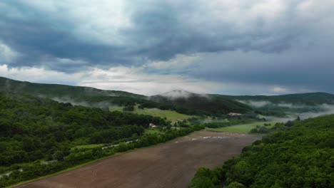 Cars-Travelling-With-Low-Fog-And-Clouds-On-Green-Mountain-Under-Dark-Sky---aerial-wide-shot