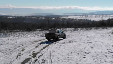 Pickup-Truck-With-Load-In-Open-Cargo-Area-Driving-On-Snowy-Road-In-Bulgaria-During-Winter---tracking-drone-shot