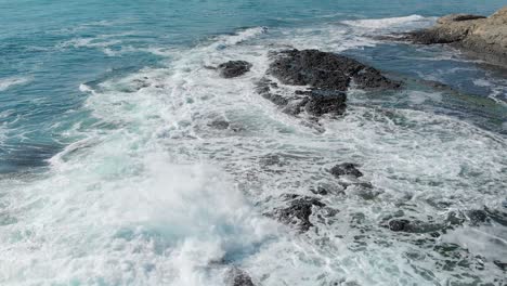 Turquoise-waves-rolling-over-black-rock--aerial