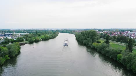 Aerial-drone-view-following-a-freight-transport-ferry,-Inland-waterway-shipping-on-Main-river,-in-Germany