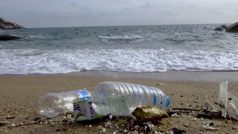 Littered-plastic-bottles-littered-in-beachfront-near-rushing-wave,-slow-zoom-in-steady-shot