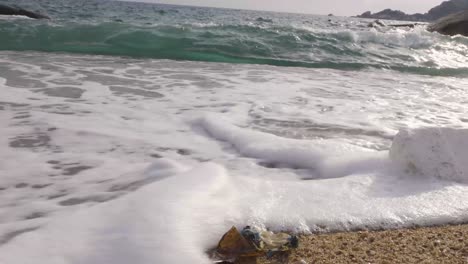 Hush-wave-washing-over-plastic-trash-on-beach,-Low-angle-parallel-static-4K-side-shot