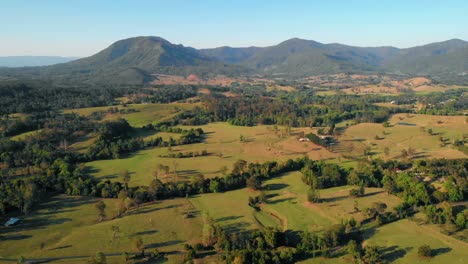 Aerial-view-of-fields-and-trees,-towards-mountains,-sunny-day,-on-the-countryside-of-Nimbin,-Australia---dolly,-drone-shot