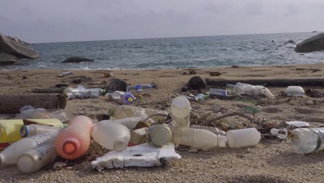 Lots-of-plastic-bottles-littered-in-beachfront-near-continuous-rushing-wave,-static-shot-4k