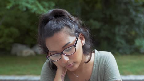 Portrait-Of-Pretty-Girl-With-Glasses-Feeling-Sad-Outdoors-At-Park,-Puts-Head-Down-On-Hand-In-Disappointment-Showing-Emotions