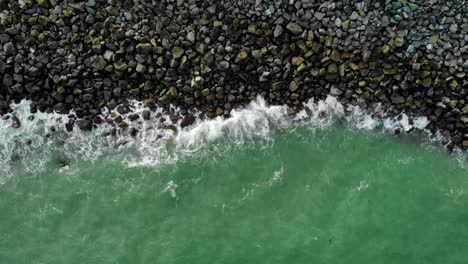 Aerial-view-above-turquoise-waves-washing-over-a-rocky-coast,-in-Mackay,-Australia---top-down,-drone-shot