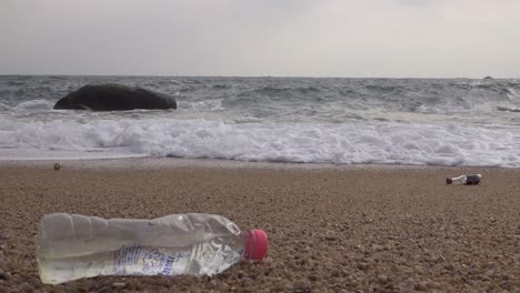 A-littered-plastic-bottle-left-on-beach-washing-by-waves,-steady-stable-shot